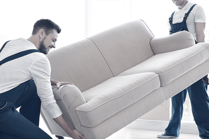Two workers carry out furniture transport and assembly services by moving a sofa